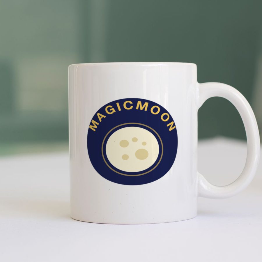 White ceramic mug on a table with a full moon design and the word MAGICMOON curved around it printed on the side